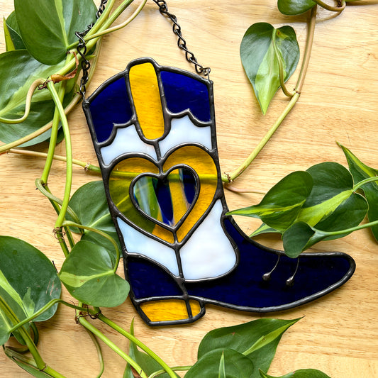 Blue and yellow stained glass cowboy boot on a wooden surface with plants