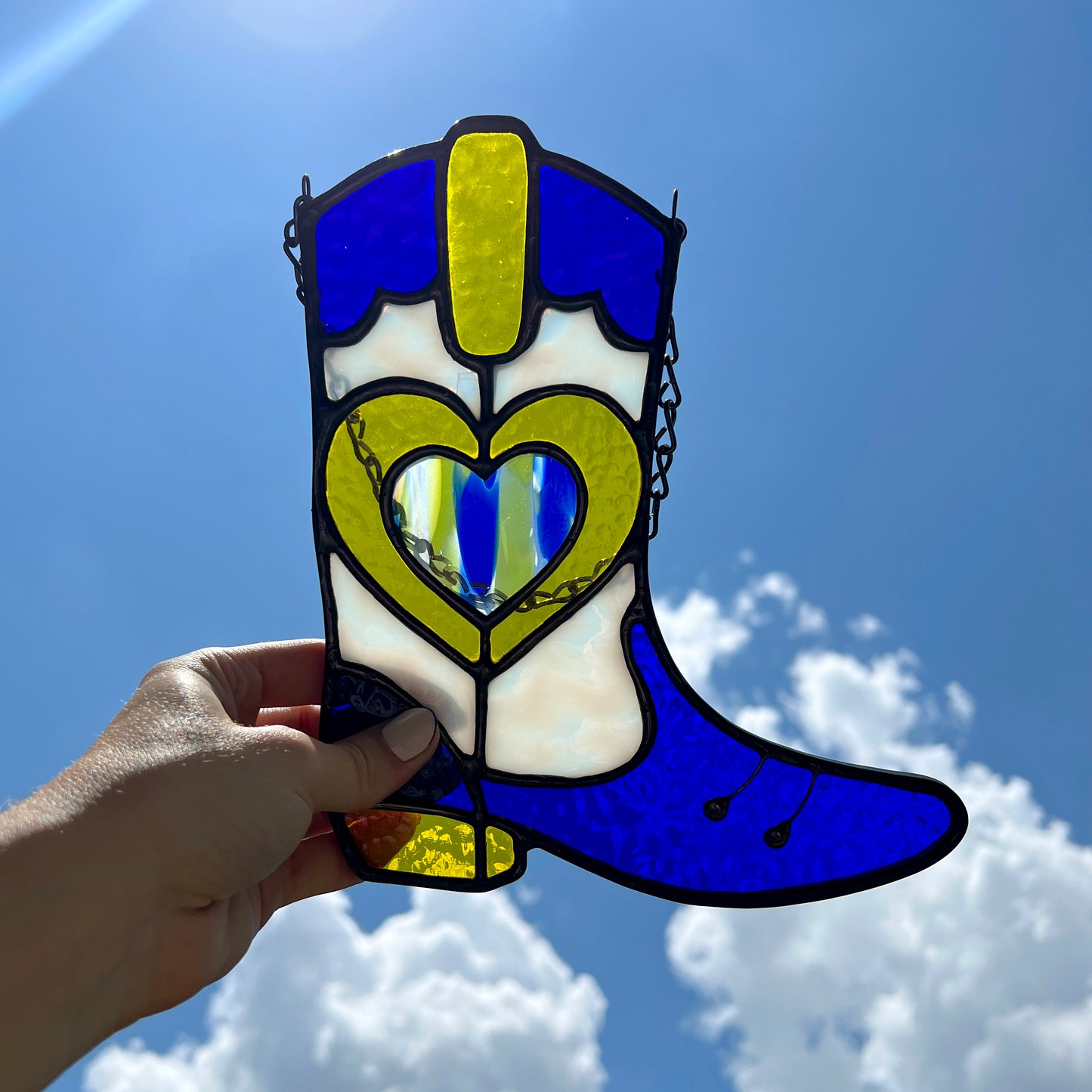 Backlit Blue and yellow stained glass cowboy boot with the sky behind