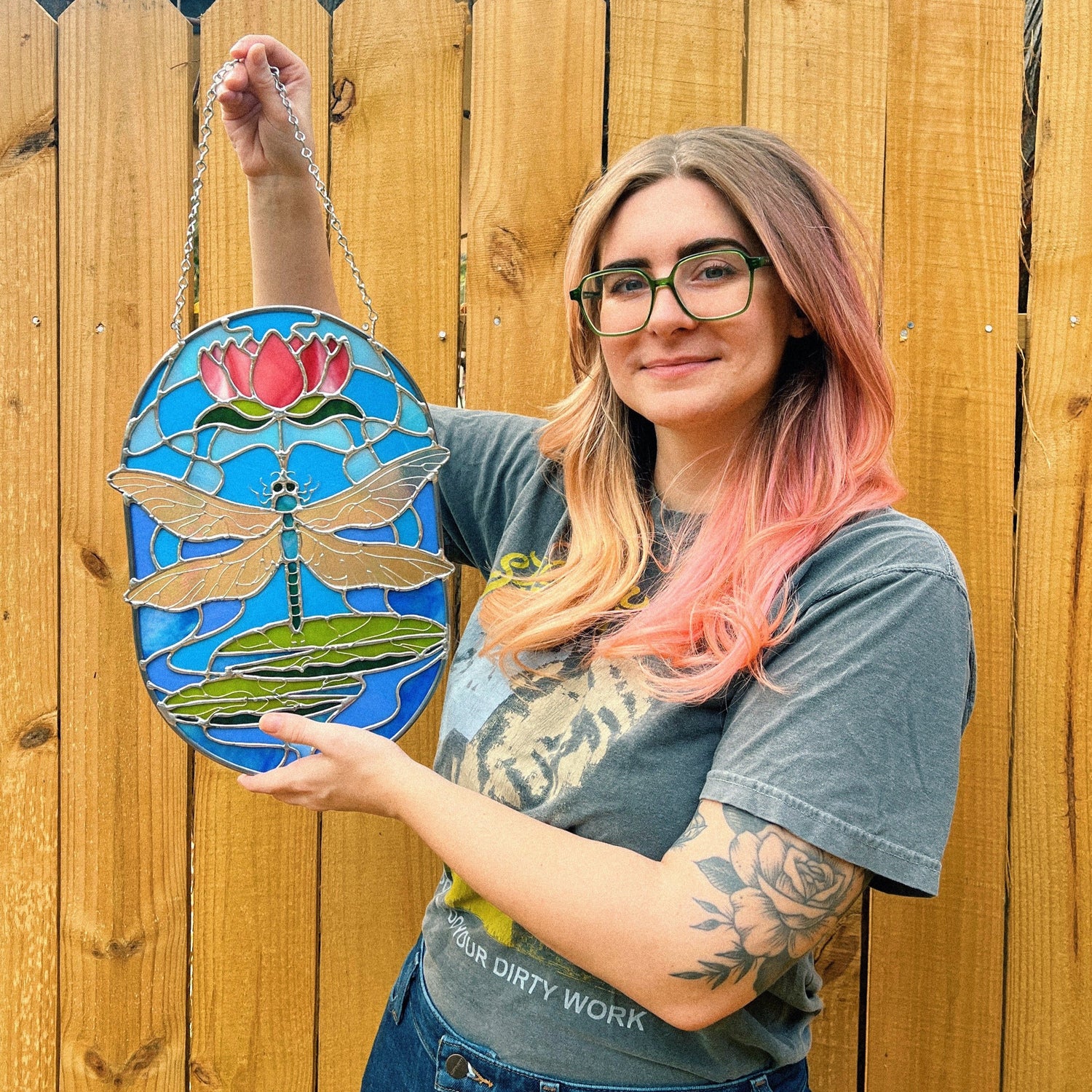 Giorgie holding a custom commission stained glass piece of an art nouveau-styled dragonfly